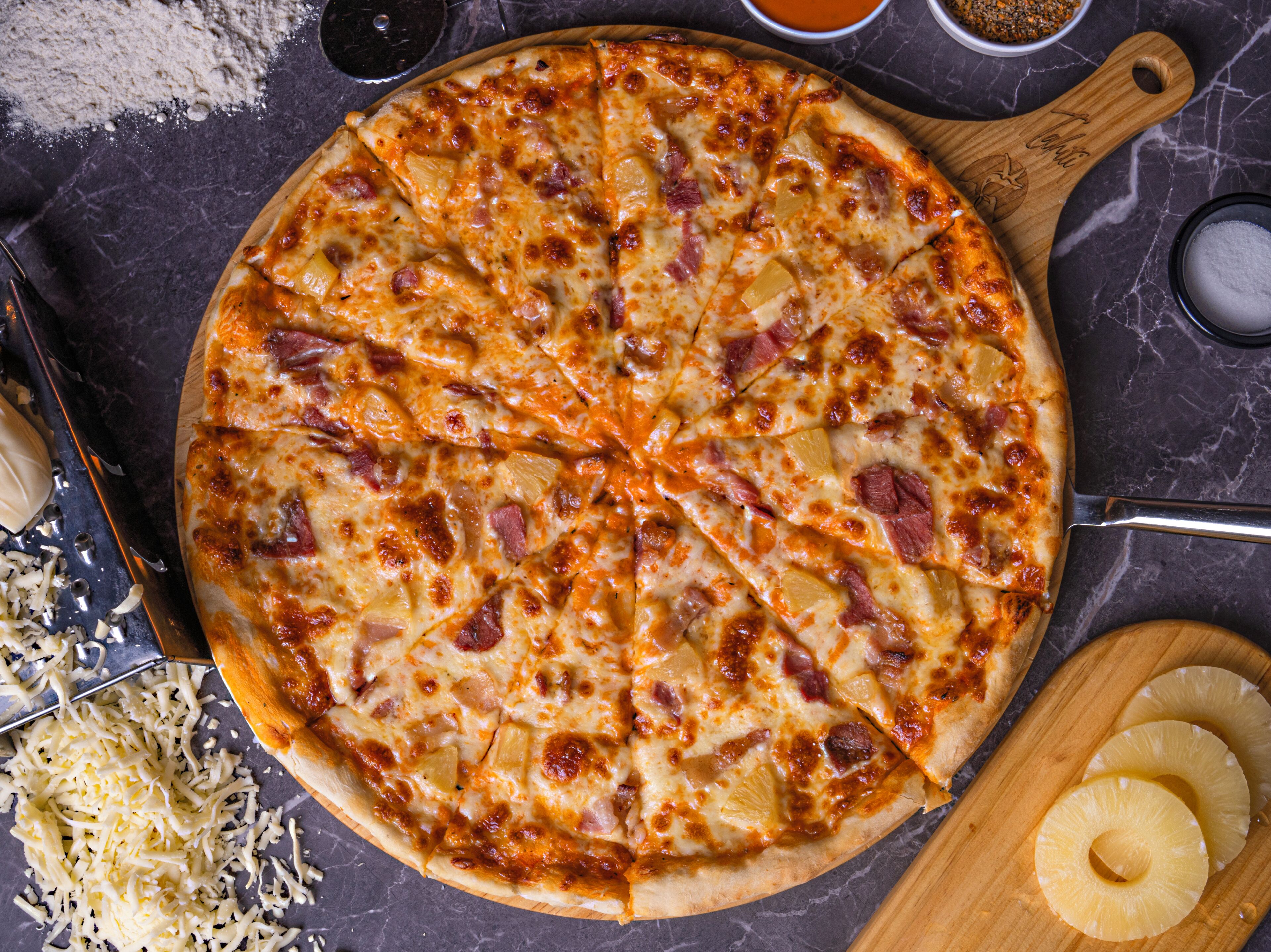 A pizza with pineapple and ham toppings on a wooden board.