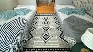 A compact hotel room with two single beds, a central rug, a washing machine, and a kitchenette.