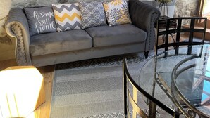 Ein gemütlicher Wohnbereich mit Steinwand, grauem Sofa mit gemusterten Kissen, Glastisch und Teppich mit Muster.
