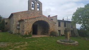 Eine alte Steinkirche mit einem Glockenturm, einem Rundbogenportal und einem kleinen Garten mit einem Brunnen.