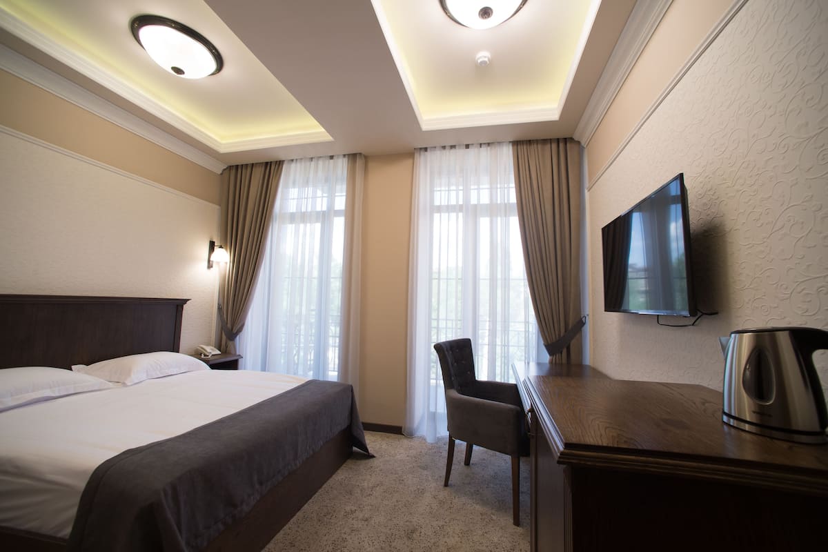 Une chambre d’hôtel avec un grand lit, un bureau avec une bouilloire, une télévision à écran plat et une chaise.