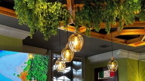 A restaurant interior with hanging plants, a bar counter, and a large window displaying a coastal view. - Boulevard Hotel (Yerevan)