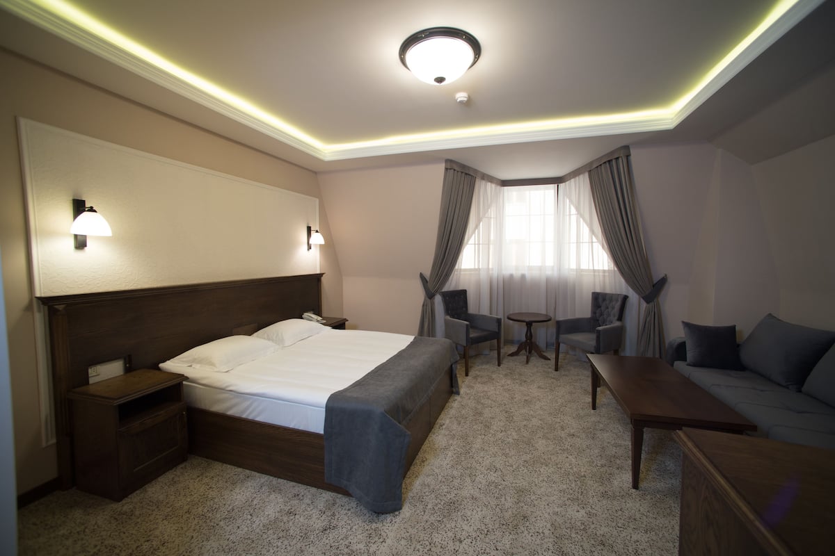 Une chambre d’hôtel comprenant un lit, des tables de chevet, un bureau, une chaise, un canapé et une fenêtre avec des rideaux.
