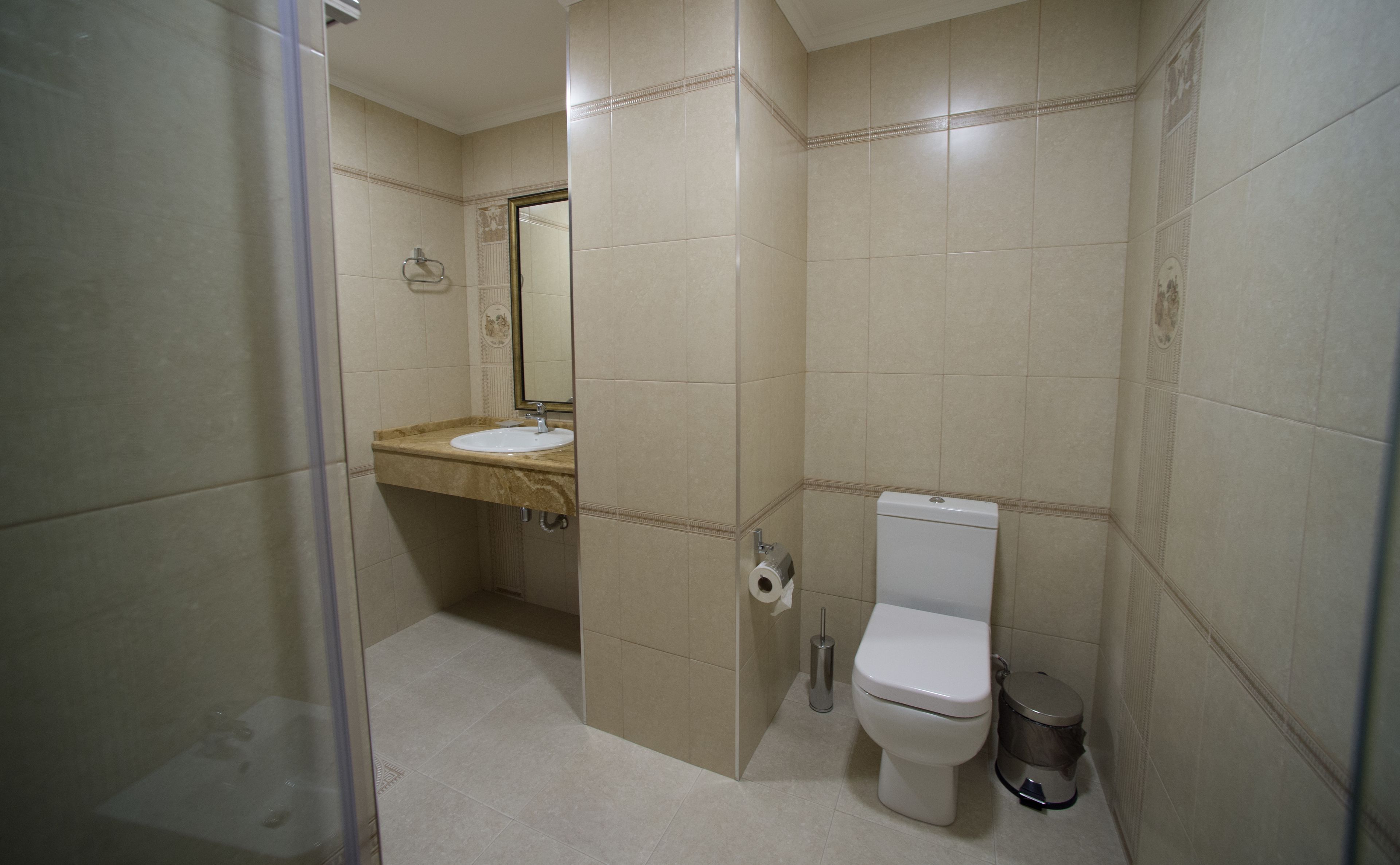 A bathroom with a sink, toilet, and trash can.