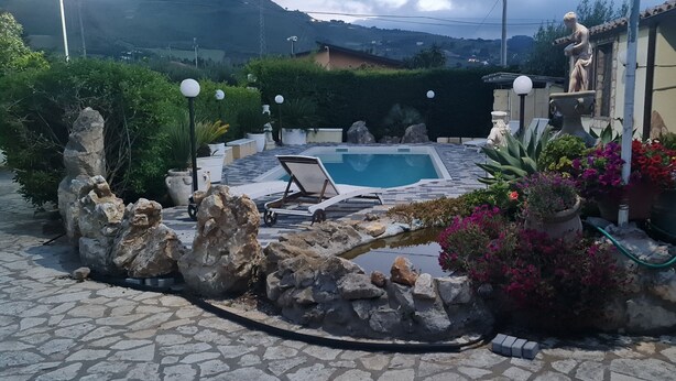 Una piscina de piedra con sillas de descanso, rodeada de rocas y plantas en macetas.