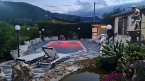 Una piscina con una luz roja, rodeada de sillas de descanso y plantas en macetas.