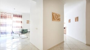 Un hall d’entrée spacieux, avec une table et des chaises en verre, un rideau à motifs et des œuvres d’art murales.