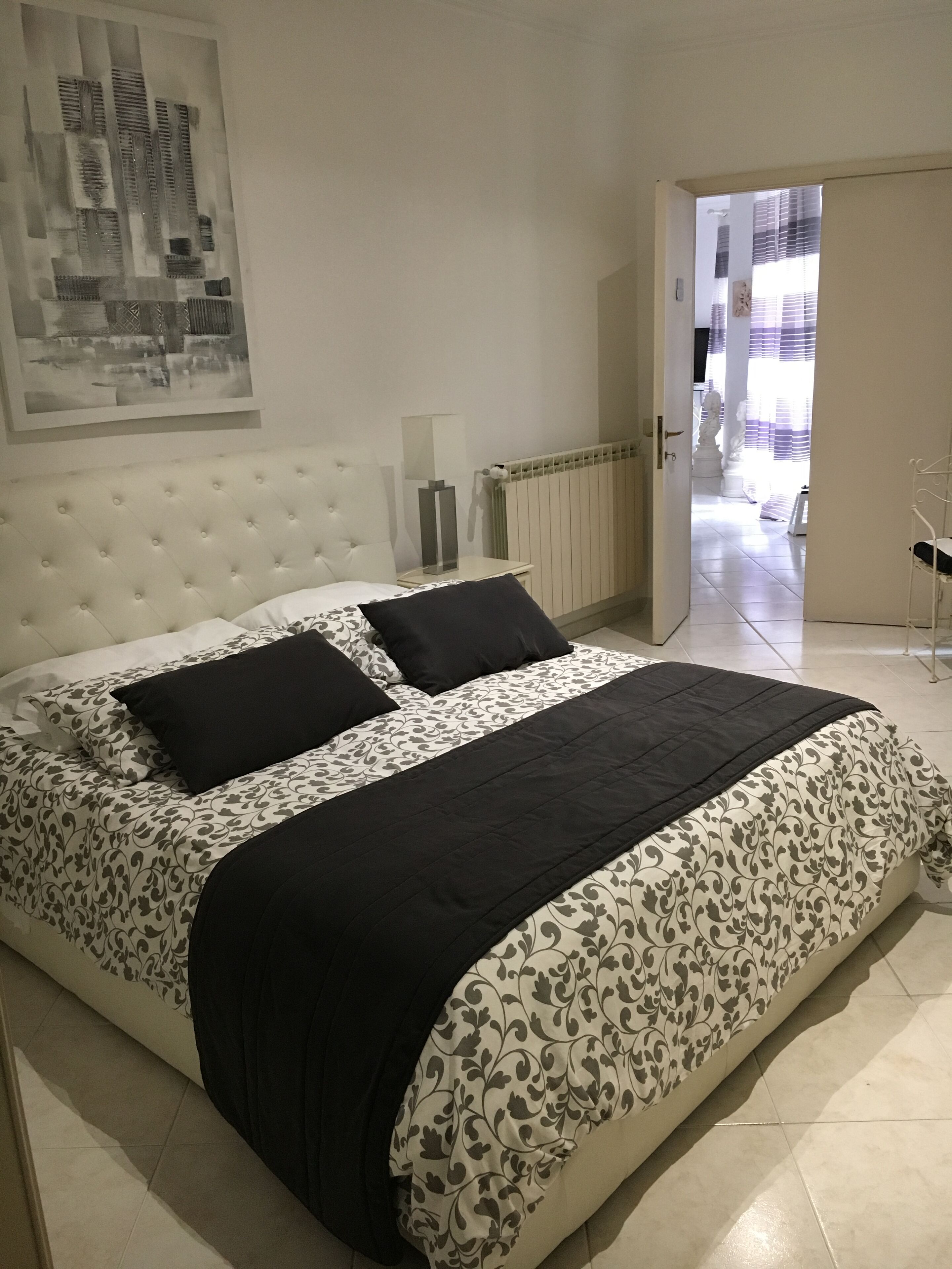 A neatly made bed with a floral-patterned duvet and black pillows, a white headboard, and a framed picture on the wall.