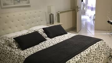 A neatly made bed with a floral-patterned duvet and black pillows, a white headboard, and a framed picture on the wall.