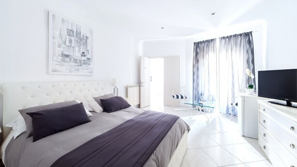Une chambre à coucher moderne, dotée d’un grand lit, d’un téléviseur à écran plat et d’une œuvre d’art représentant un paysage urbain accrochée au mur.