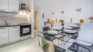 Une cuisine moderne avec des meubles blancs, une cuisinière à gaz et une table à manger en verre pour quatre personnes.