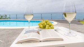 A poolside setting with two wine glasses, a plate of grapes, and an open book. - Sea View, Luxury, Comfort, Privacy, Free Wifi and Heated Pool (Arco da Calheta)