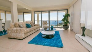 A spacious living room with a beige sofa, a round coffee table, and a large window offering a view of the sea. - Sea View, Luxury, Comfort, Privacy, Free Wifi and Heated Pool (Arco da Calheta)