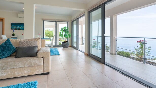 A spacious living room with a beige sofa, a large window, and a potted plant. - Sea View, Luxury, Comfort, Privacy, Free Wifi and Heated Pool (Arco da Calheta)