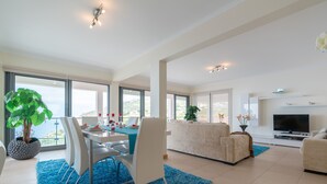 A modern living room with a dining area, large windows, a flat-screen TV, and a potted plant. - Sea View, Luxury, Comfort, Privacy, Free Wifi and Heated Pool (Arco da Calheta)