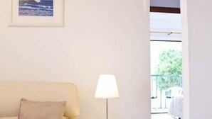 Un salon avec un canapé beige, une petite table blanche surmontée d’une lampe, et un tableau encadré accroché au mur.