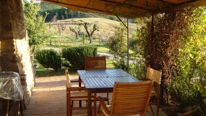 Portico coperto con tavolo e sedie, affacciato su un paesaggio collinare con alberi e una recinzione.