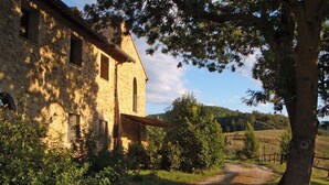 Un edificio in pietra rustica con un sentiero sterrato che vi conduce, immerso nel verde e circondato da alberi.