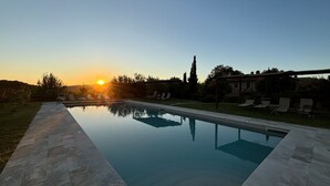 Una piscina rettangolare con una superficie speculare, circondata da un solarium in pietra e da una zona verde.
