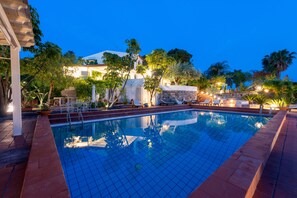 Una piscina con solárium empedrado, rodeada de sillas de descanso y plantas en macetas.