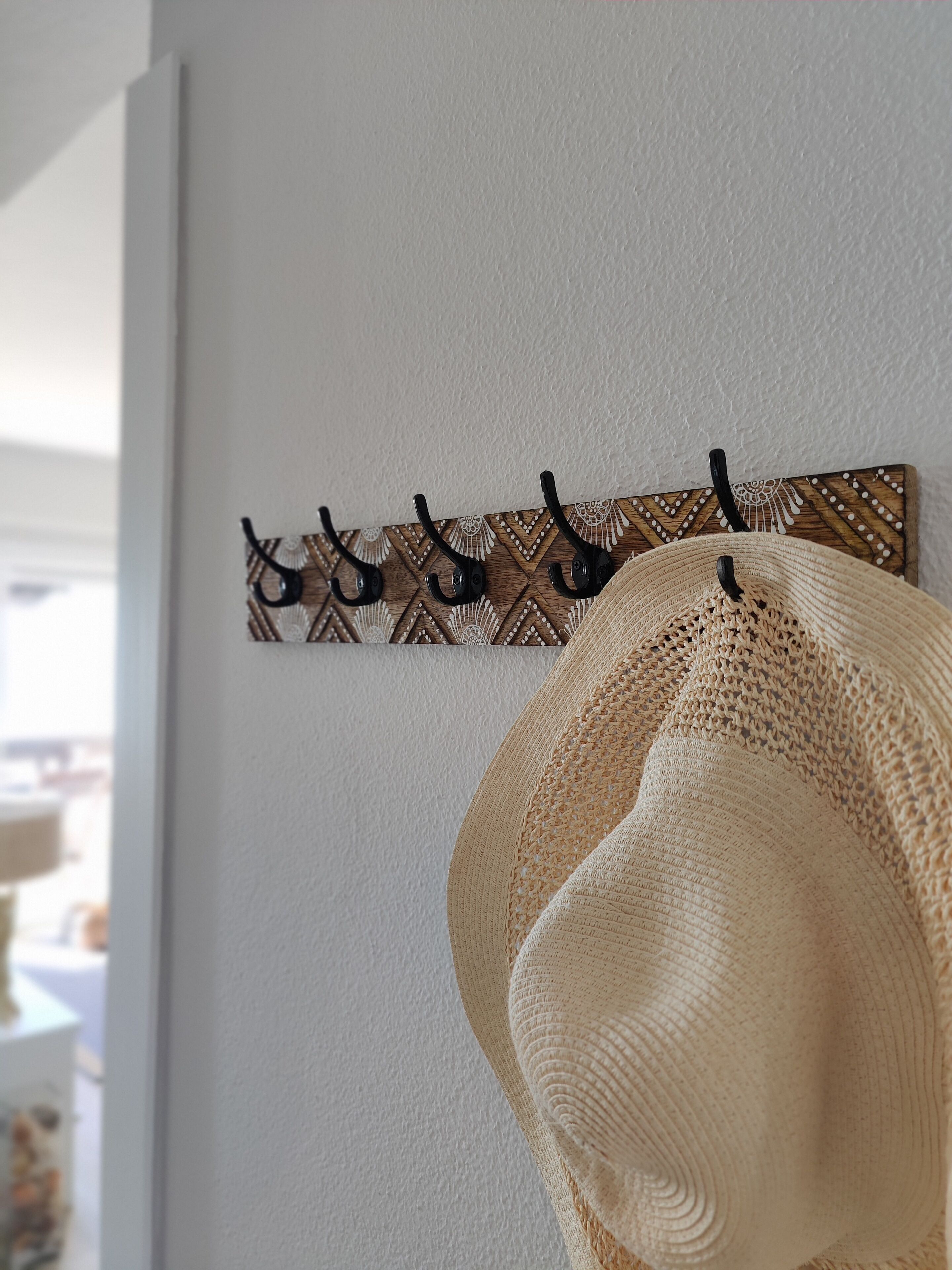 A wall-mounted wooden panel with a geometric pattern and black hooks.