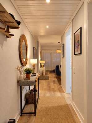 Un couloir avec un banc en bois, un miroir, une table avec une lampe et une chaise.