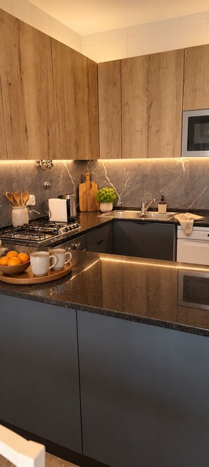 Une cuisine moderne avec des meubles en bois, une cuisinière à gaz, un évier et un plan de travail agrémenté d’une planche à découper et d’une plante.