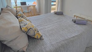 Un dormitorio con una cama grande, un ordenador portátil sobre una mesita y vistas al océano a través de la ventana.