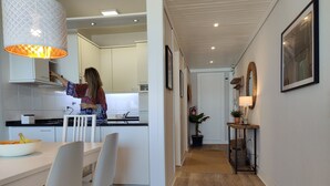 Una cocina moderna con armarios blancos, un comedor con mesa y sillas blancas, y un pasillo con piso de madera.