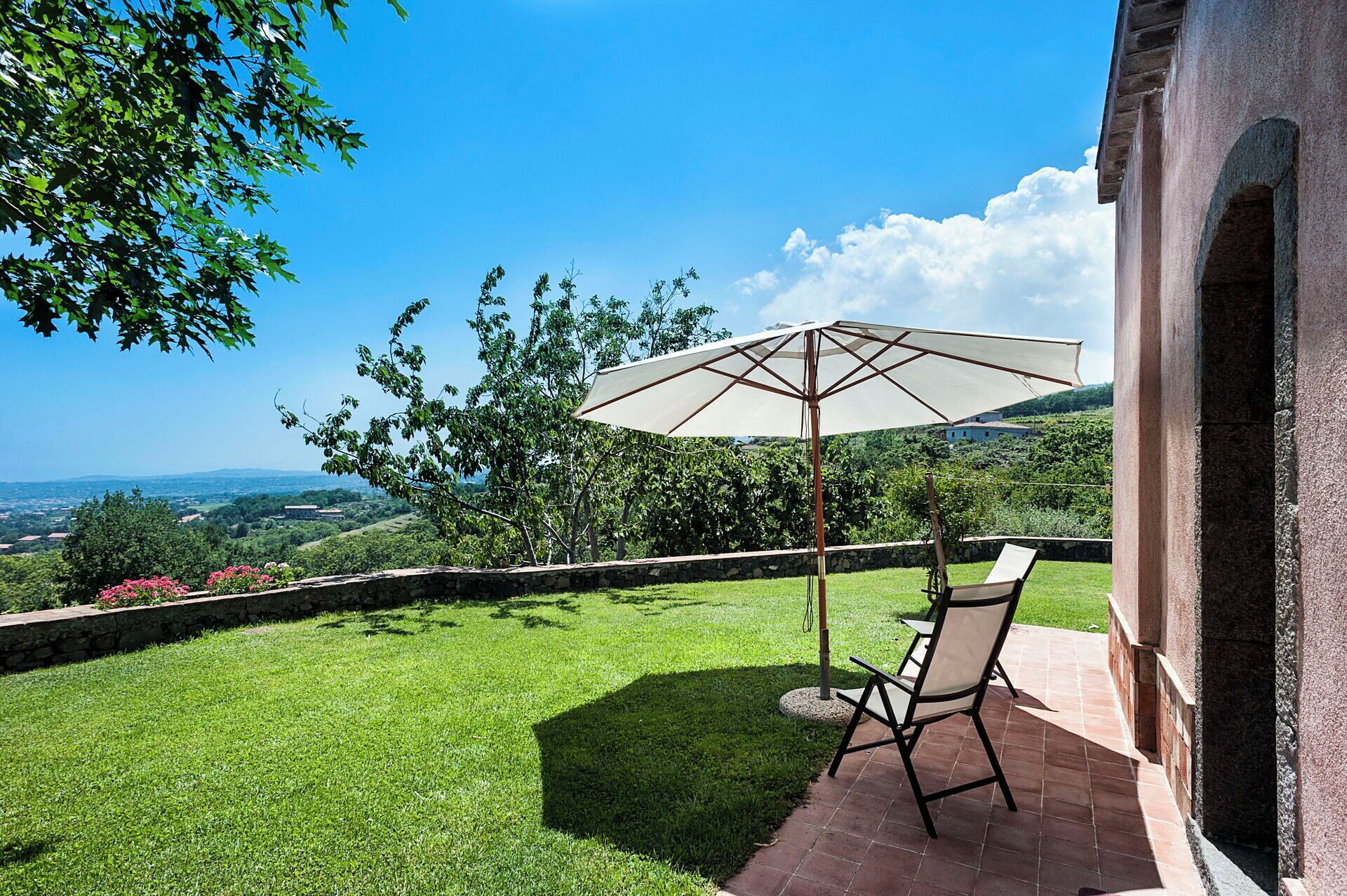 Un patio con una mesa, una silla, un paraguas y un muro de piedra.