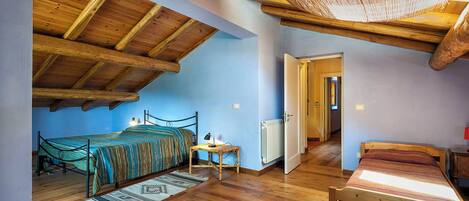 A bedroom with a sloped ceiling, wooden beams, two beds, a small table, and a radiator.