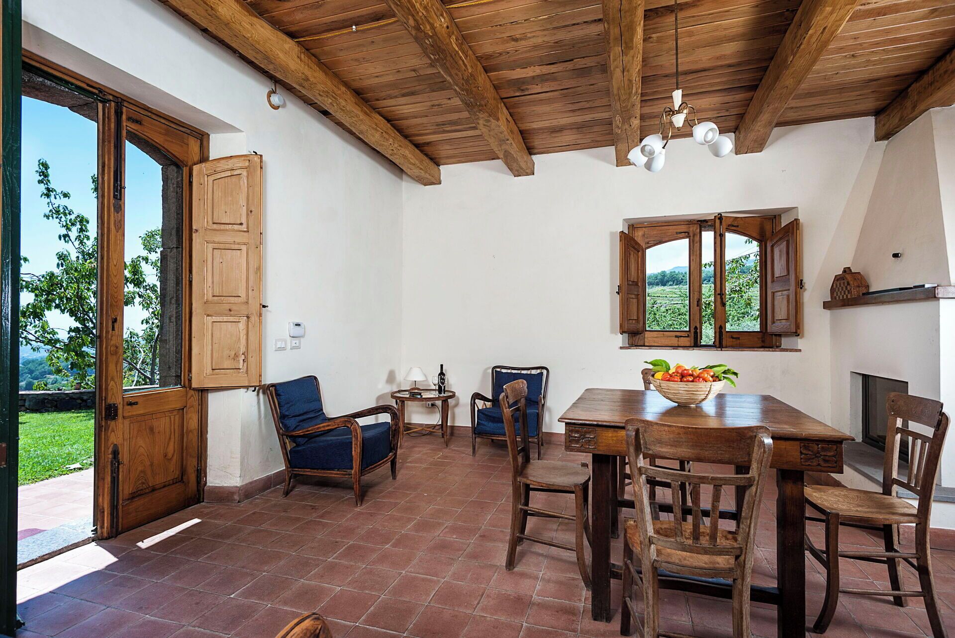 A rustic dining area with wooden furniture, a tiled floor, and a view of greenery outside.