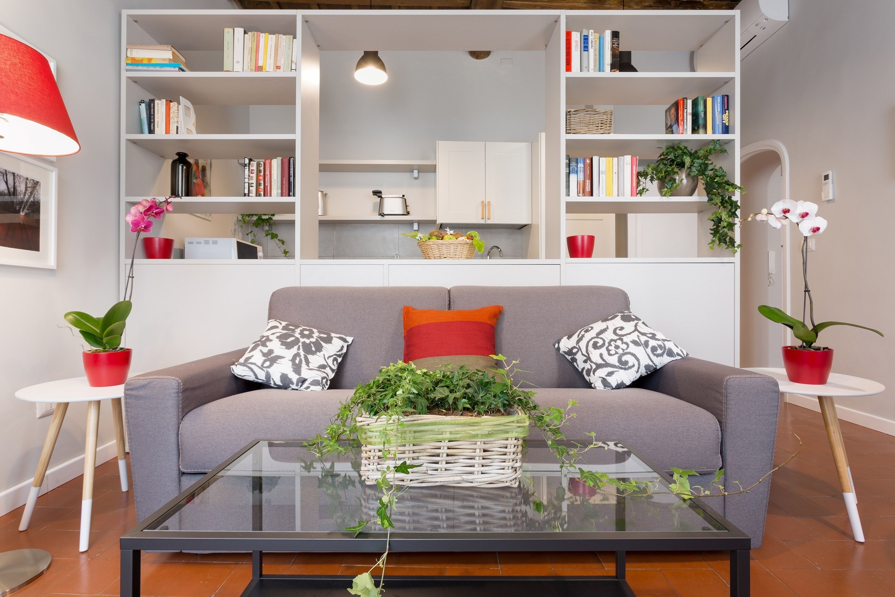 A modern living room with a grey sofa, a glass coffee table, and a bookshelf filled with books and decorative items.