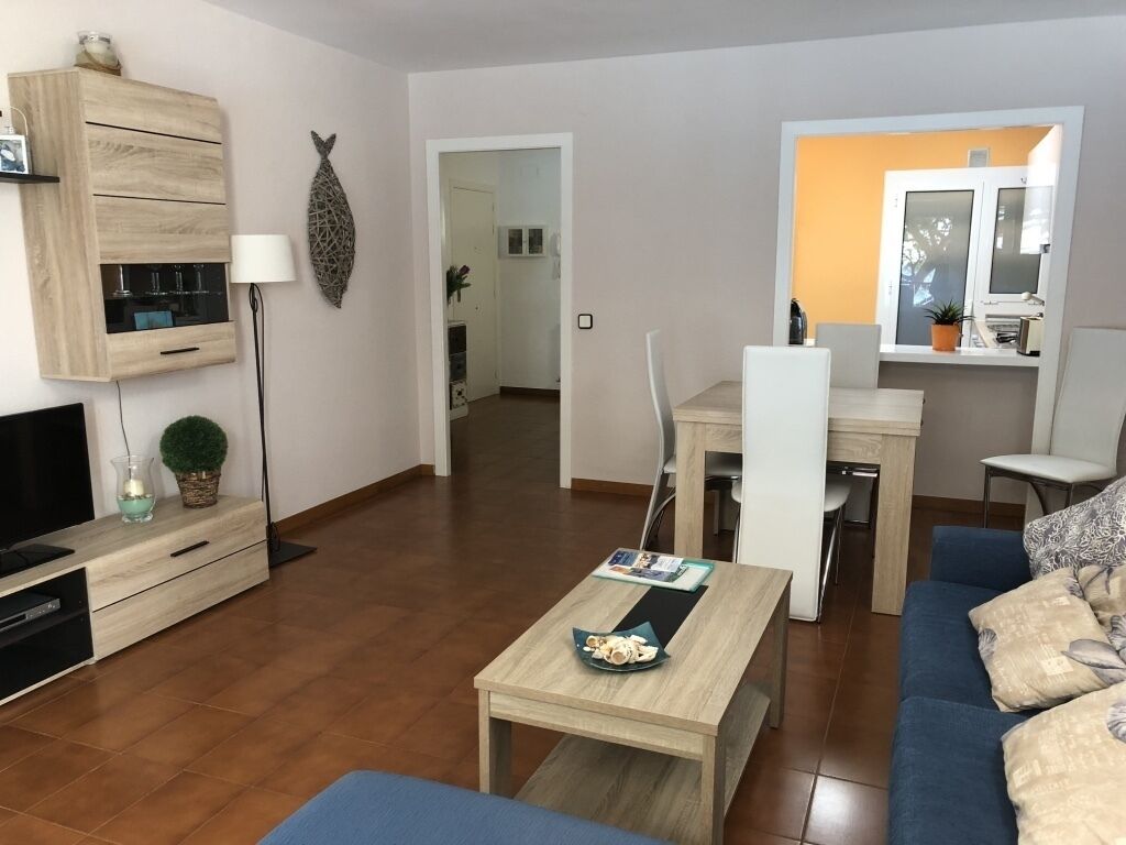 A modern living room with a sofa, coffee table, TV, and a dining area with chairs and a table.