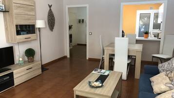A modern living room with a sofa, coffee table, TV, and a dining area with chairs and a table.
