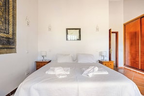 Une chambre d’hôtel avec un grand lit, deux tables de chevet, une armoire en bois et un tableau accroché au mur.