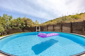 A clear blue swimming pool with a wooden fence, a ladder, and a purple floating mat.