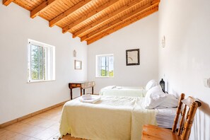 Ein Schlafzimmer mit zwei Betten, Holzbalken an der Decke und Fenstern mit Blick auf Grünflächen.