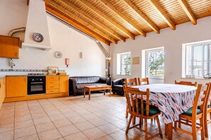 Una cocina amplia con armarios de madera y horno integrado, un comedor con mesa y sillas, y una sala de estar con sofá y lámpara.