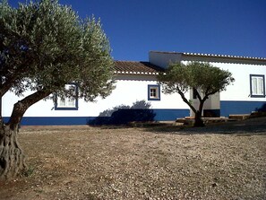 A building with a white exterior and blue trim, a tiled roof, and a gravel ground.