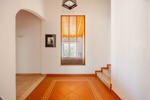 Ein Flur mit Fliesenboden, einer Holztreppe und einem Fenster mit Jalousien.