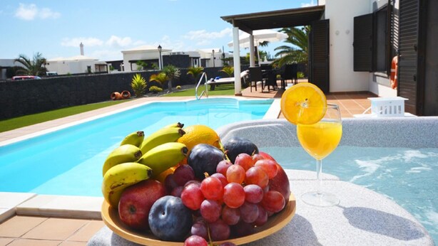A poolside setting with a fruit bowl containing bananas, grapes, and apples, and a glass of orange juice. - Luxury villa, heat pool ,ecological, chlorine-free  ,Jacutzzi / bicycl (Yaiza)