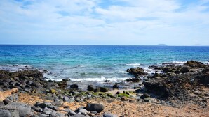 A rocky shoreline with clear blue water and a distant mountain. - Luxury villa, heat pool ,ecological, chlorine-free  ,Jacutzzi / bicycl (Yaiza)