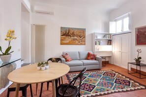 A living room with a round wooden table, a grey sofa, a patterned rug, and a painting on the wall.