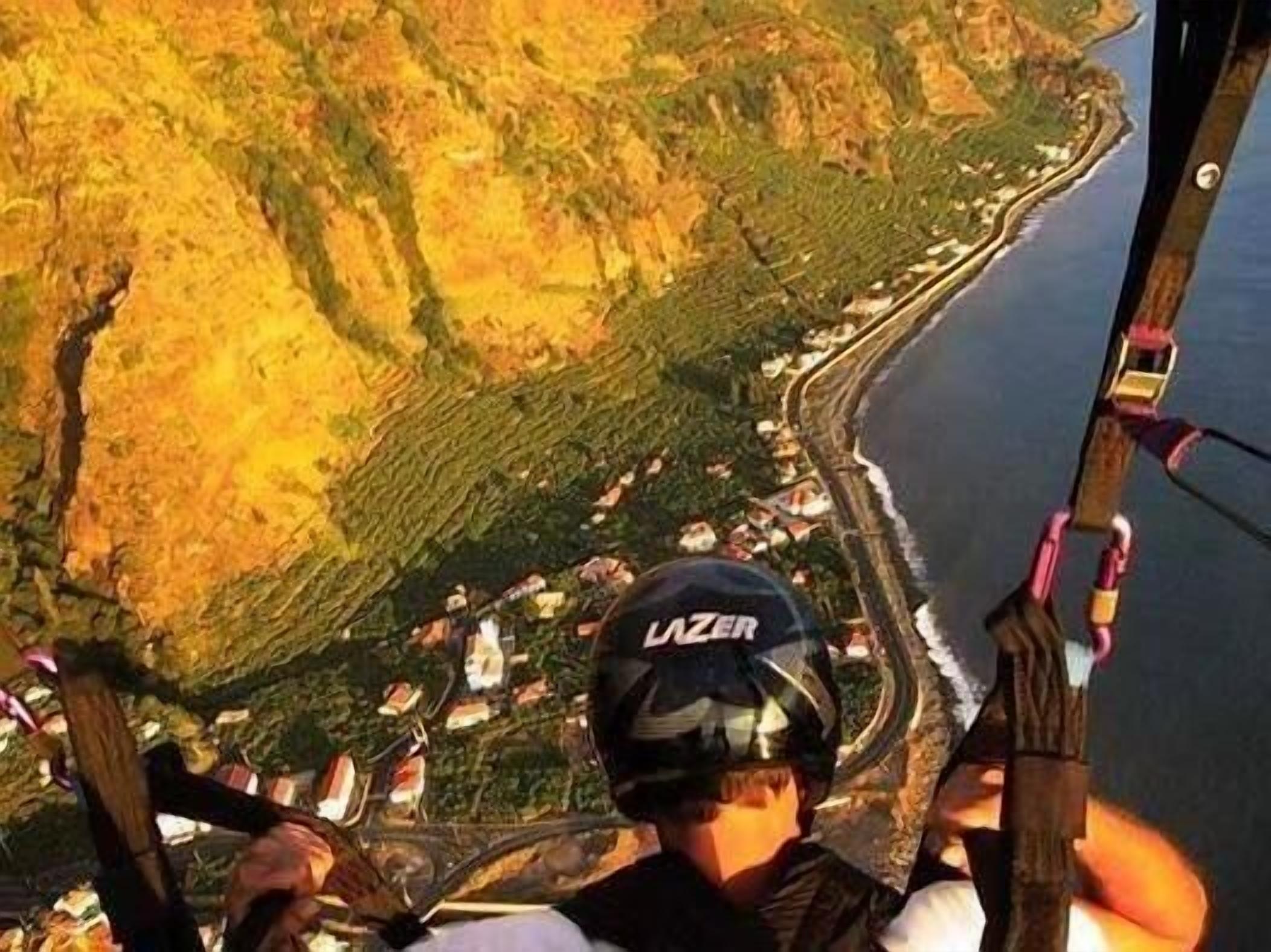 A person bungee jumping with a helmet labeled "LAZER" and a view of a coastal landscape below.