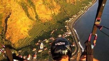 A person bungee jumping with a helmet labeled "LAZER" and a view of a coastal landscape below.