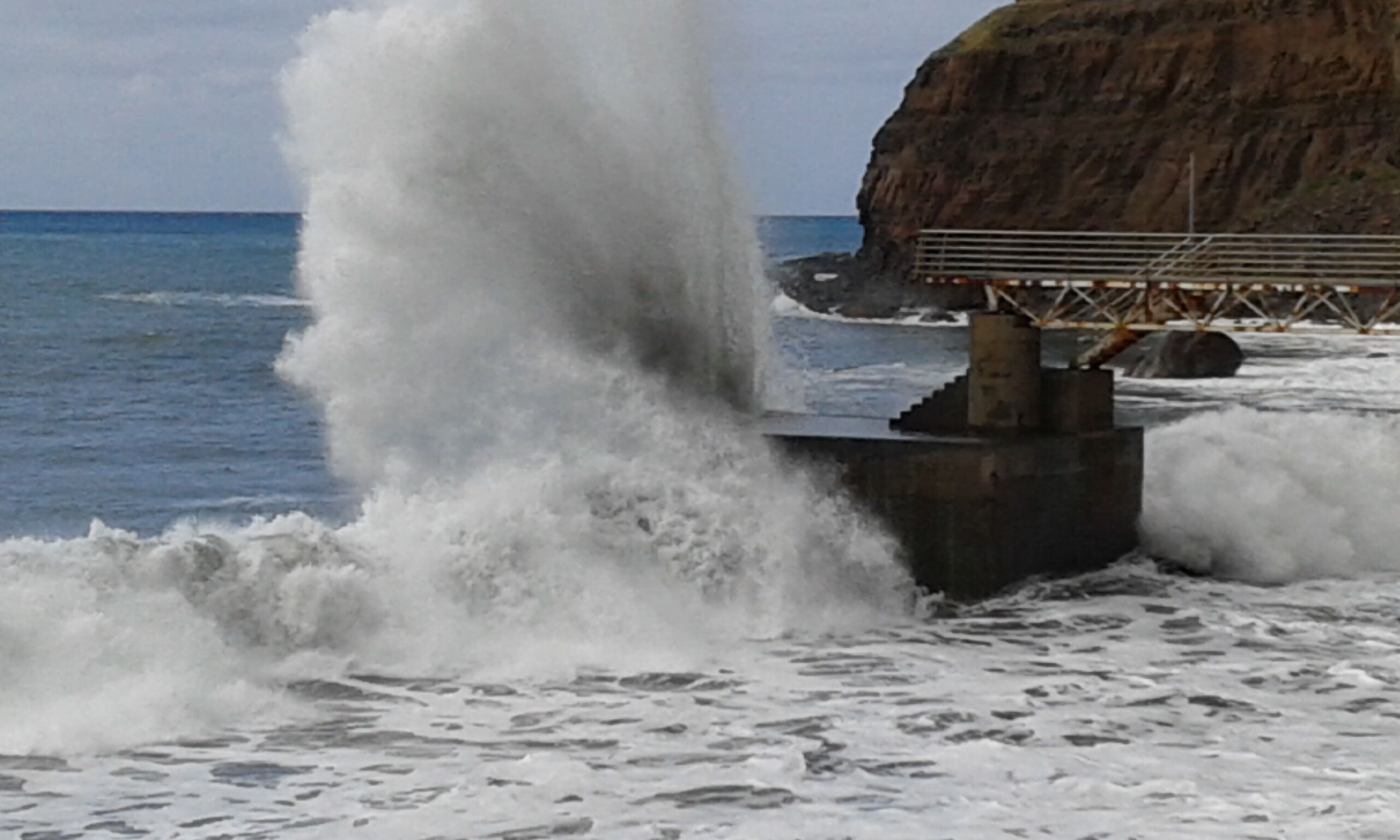 Paisaje costero con olas rompiendo contra un muro de hormigón.