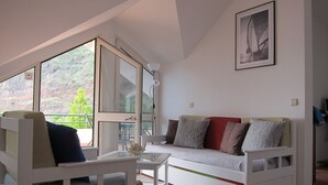 A modern living room with a sofa, a glass coffee table, and a large window offering a view of a mountainous landscape. - Marina Sol Penthouse <br>- Sea view - Free Wifi (Madalena do Mar)