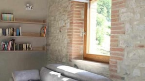 Una sala de estar moderna con un sofá gris, una estantería y una ventana con vistas a zonas verdes.