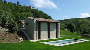 Un edificio de piedra con techo de tejas, piscina y una escalera que lleva a un nivel superior.